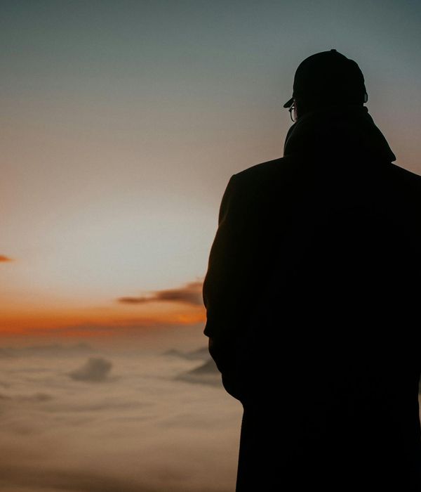 Silhouette of a person watching a sunrise over mountains.